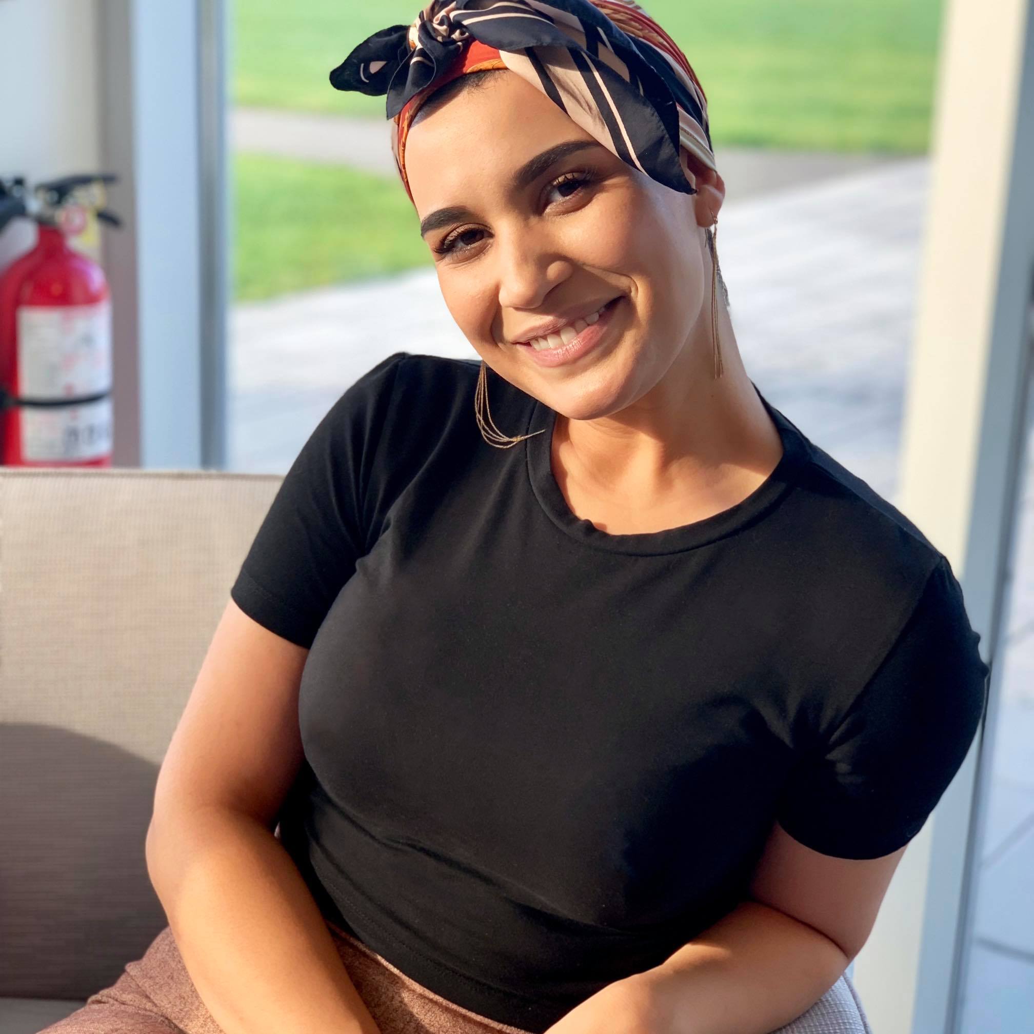 Imène Tissoukai, in a black t-shirt and patterned head scarf, smiles at the camera