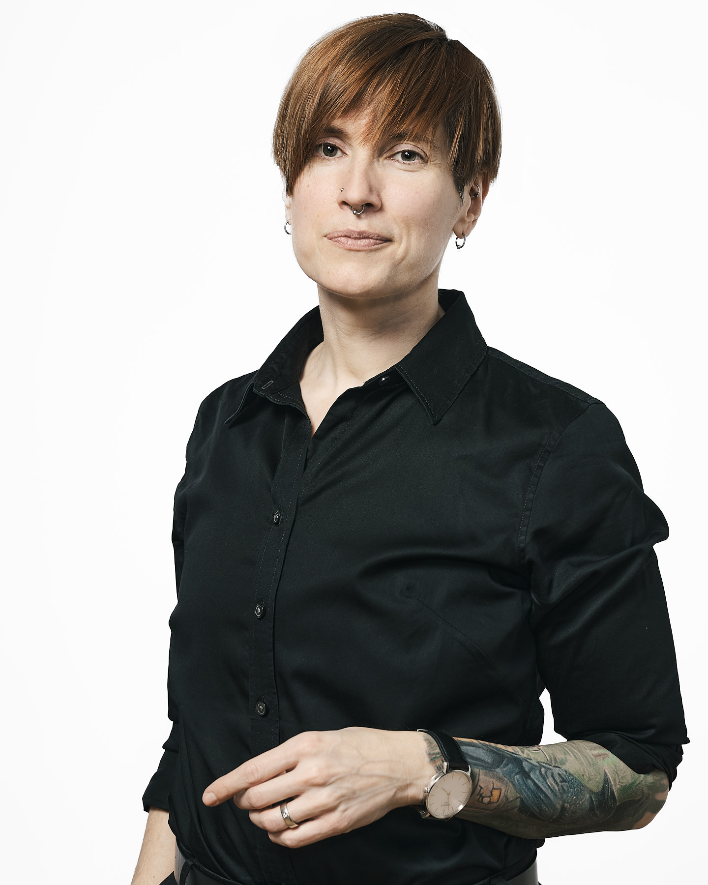 Crompton faces right in a black shirt. They have light skin, short red hair, an nose piercings